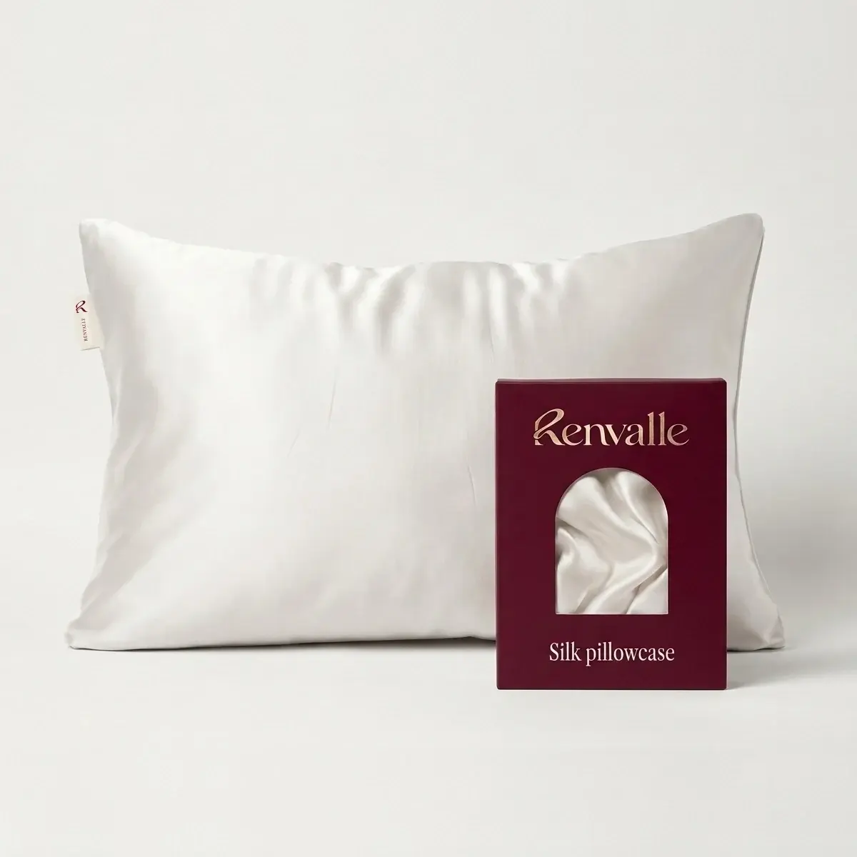 The Silk Pillowcase in Ivory on a pillow, its burgundy box in front with the folded silk showing through an arched window