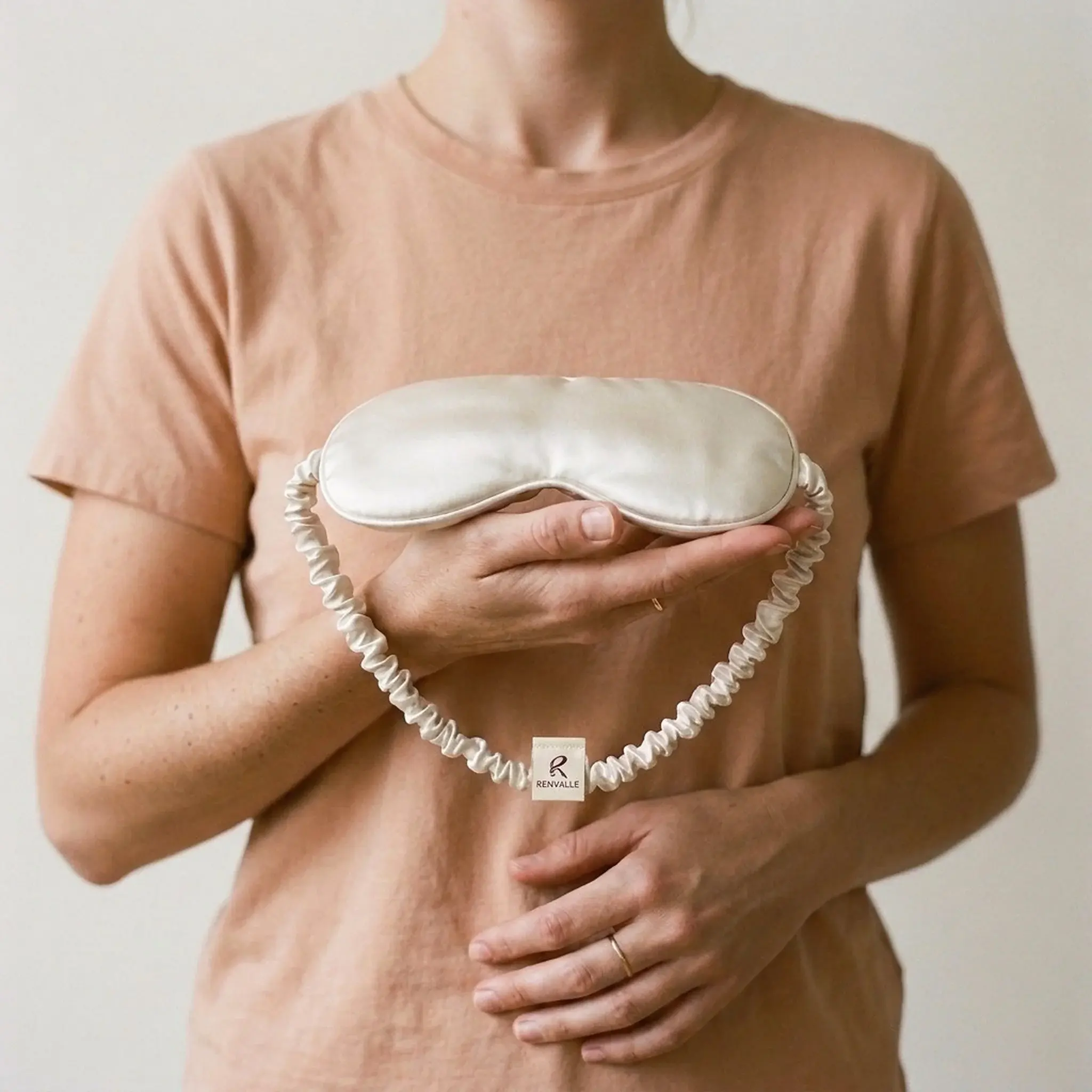 The Weighted Eye Mask in Ivory resting on an open palm, its gathered strap looped over the wrist