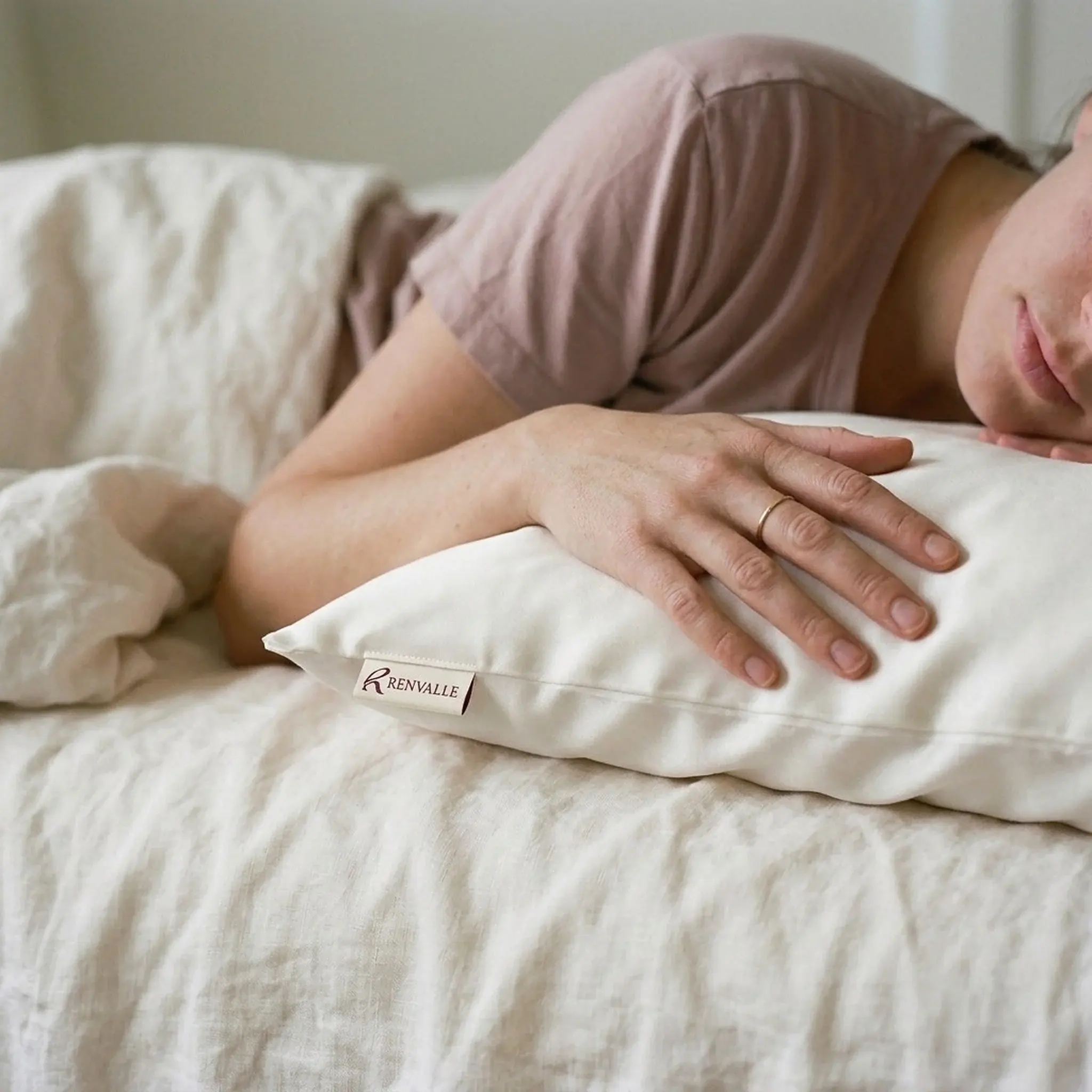 A woman lying on linen, her forearm resting on a pillow in the Ivory silk pillowcase
