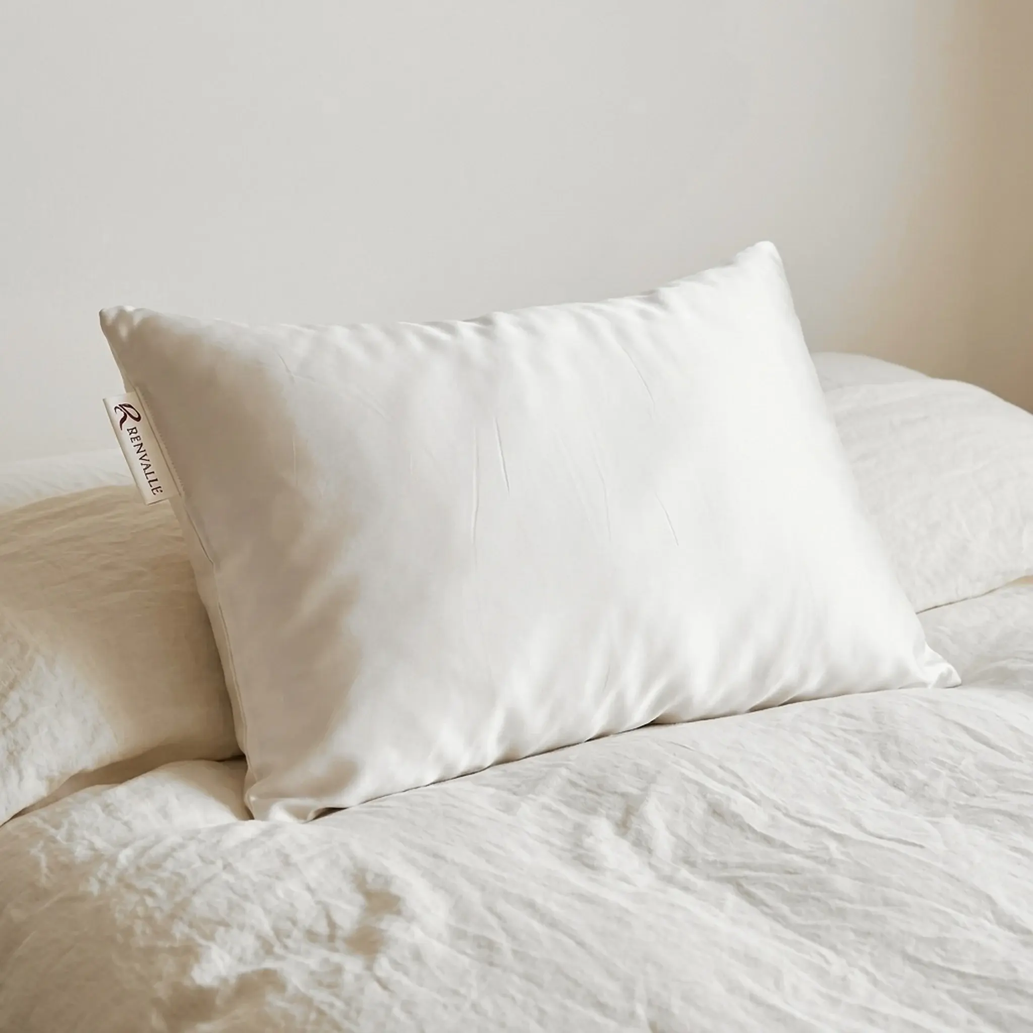 The Silk Pillowcase in Ivory on a pillow resting on a crumpled linen duvet