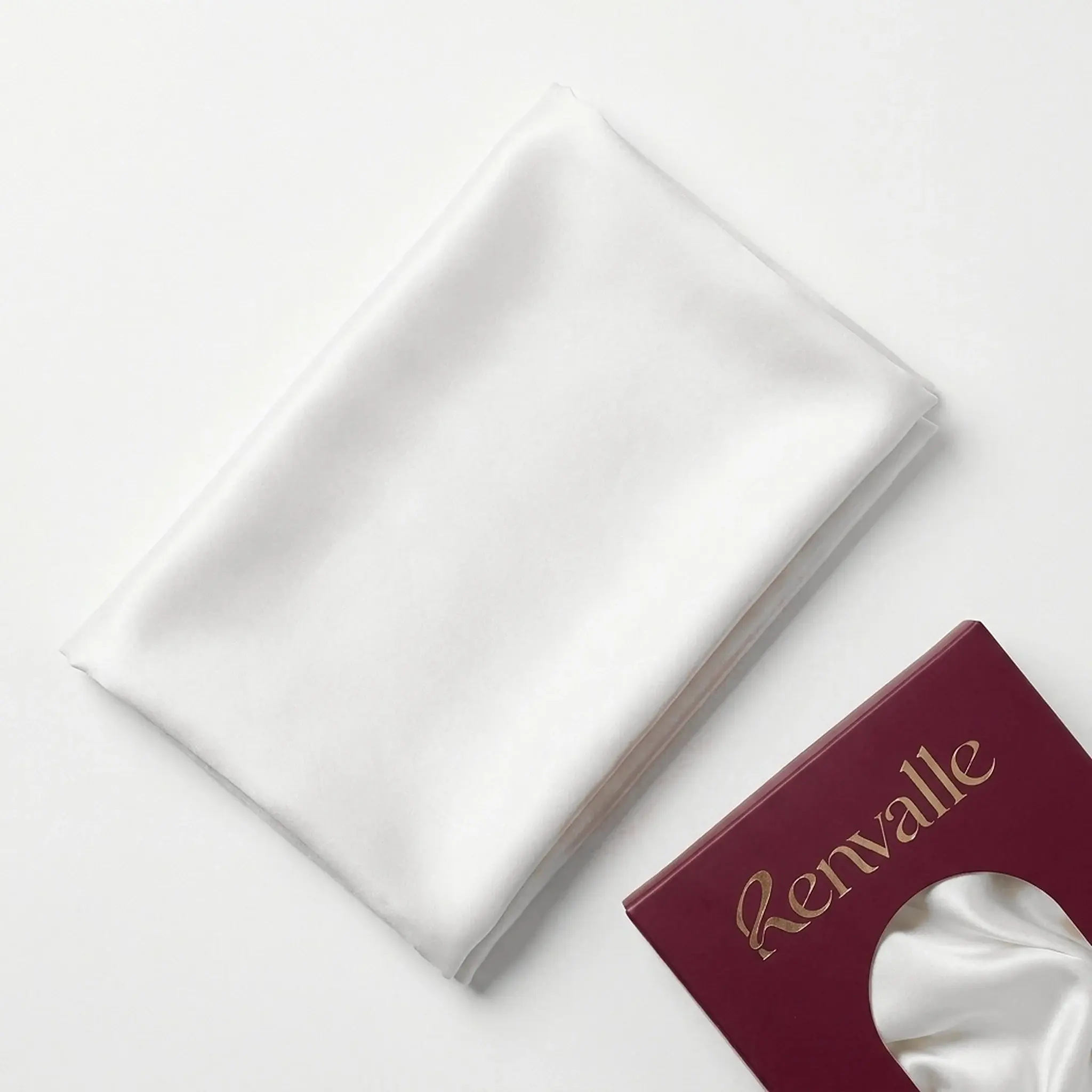 The Silk Pillowcase in Ivory, folded flat beside its burgundy box